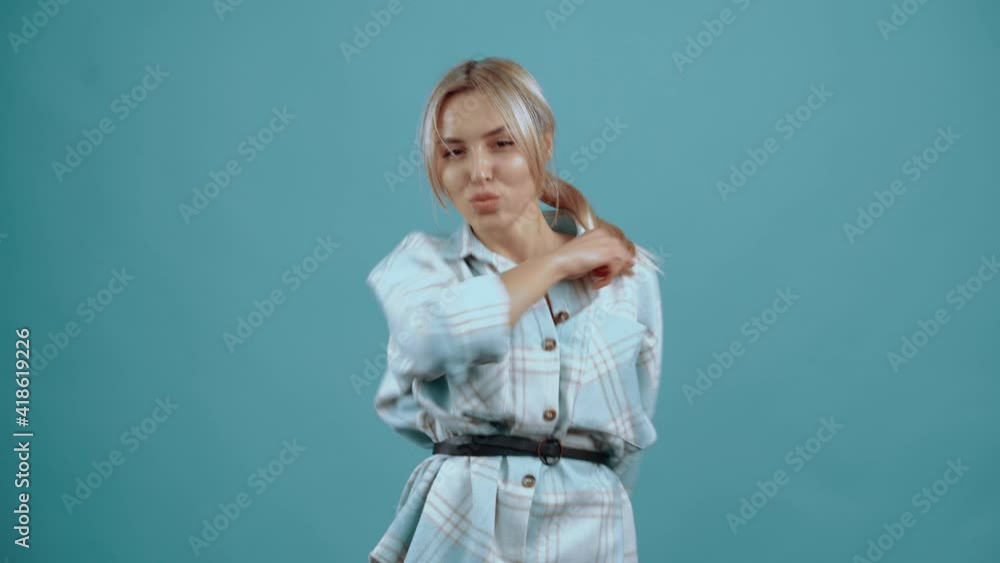 The excited and happy 20-year-old dances with her hands raised, smiles and enjoys the music. Beautiful mature young woman, blonde, in her shirt, blue. Isolated on blue background, Concept of life The excited and happy 20-year-old dances with her hands raised, smiles and enjoys the music. Beautiful mature young woman, blonde, in her shirt, blue. Isolated on blue background, Concept of life