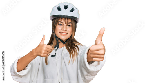 Teenager caucasian girl wearing bike helmet approving doing positive gesture with hand, thumbs up smiling and happy for success. winner gesture.