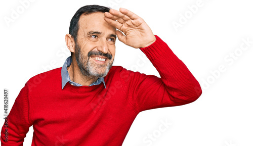 Middle age hispanic man wearing casual clothes very happy and smiling looking far away with hand over head. searching concept.