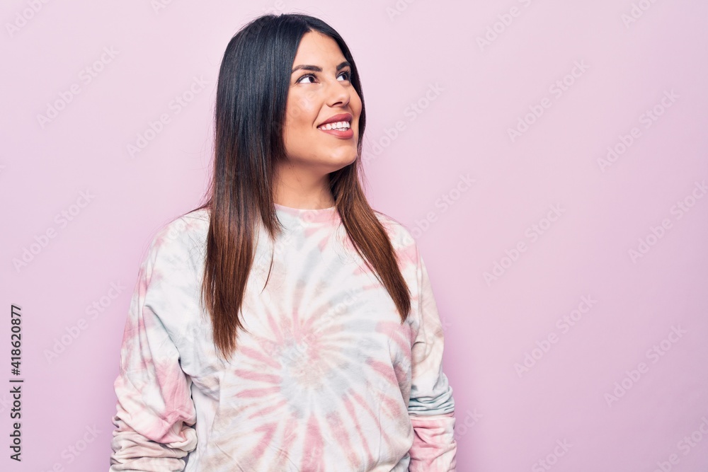 Young beautiful brunette woman wearing casual dyed sweatshirt over isolated pink background looking to side, relax profile pose with natural face and confident smile. Young beautiful brunette woman wearing casual dyed sweatshirt over isolated pink background looking to side, relax profile pose with natural face and confident smile.