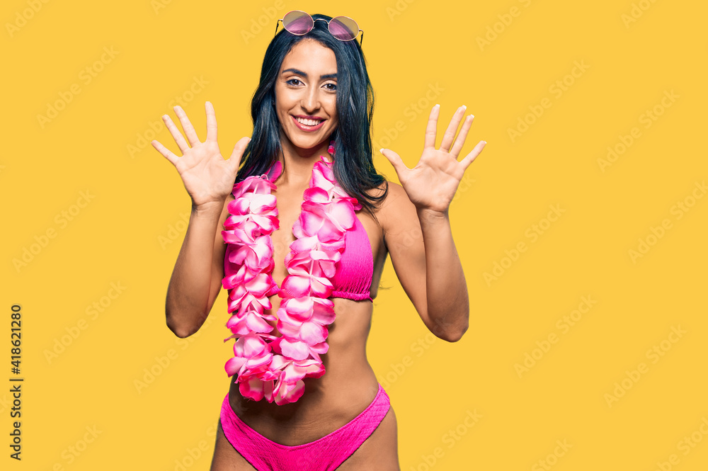Beautiful hispanic woman wearing bikini and hawaiian lei showing and pointing up with fingers number ten while smiling confident and happy. Beautiful hispanic woman wearing bikini and hawaiian lei showing and pointing up with fingers number ten while smiling confident and happy.