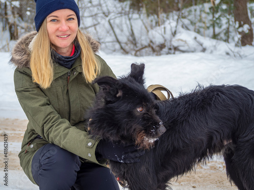 Young woman playing with funny Black pet dog with snow. on the background. Playing with the snow. Adorable dog enjoying her time, winter time. Copy space