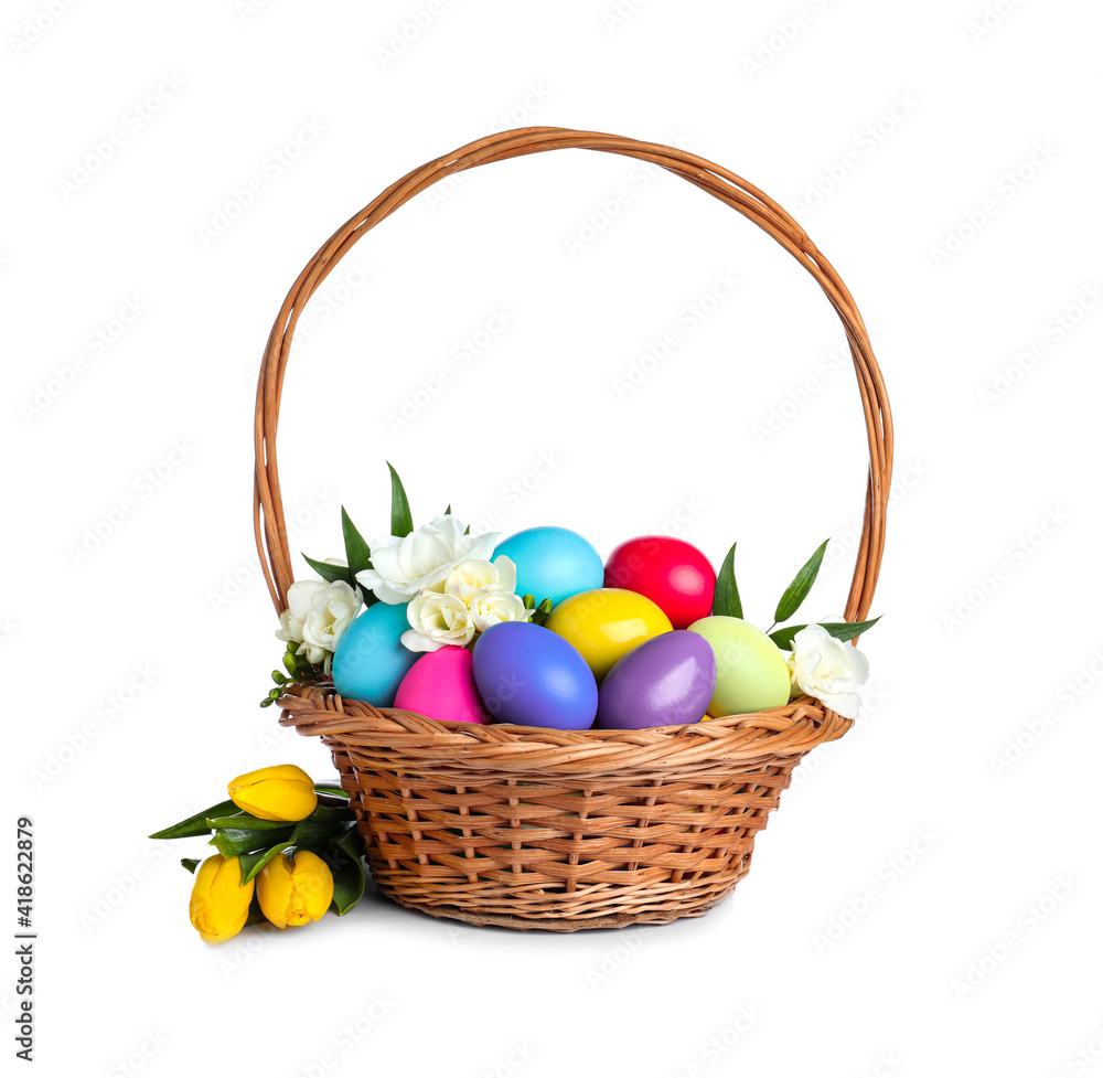 Wicker basket with bright painted Easter eggs and spring flowers on white background