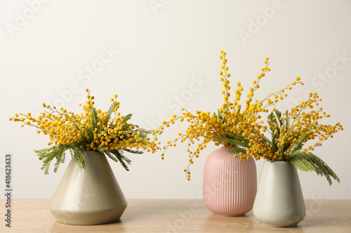 Beautiful mimosa flowers in vases on wooden table
