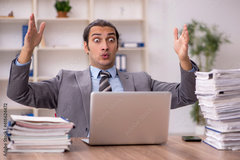 Young male employee unhappy with excessive work in the office Young male employee unhappy with excessive work in the office