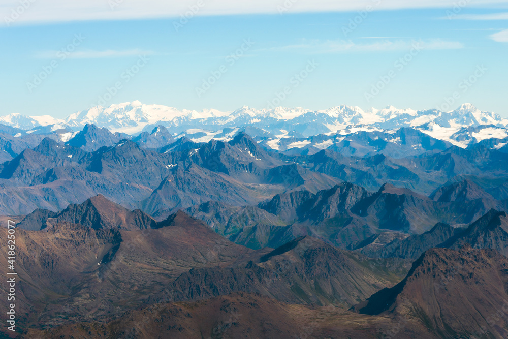 Aerial view of mountainous landscape in Alaska. Mountains with no snow in foreground and snow capped behind. Sunny day during summer.