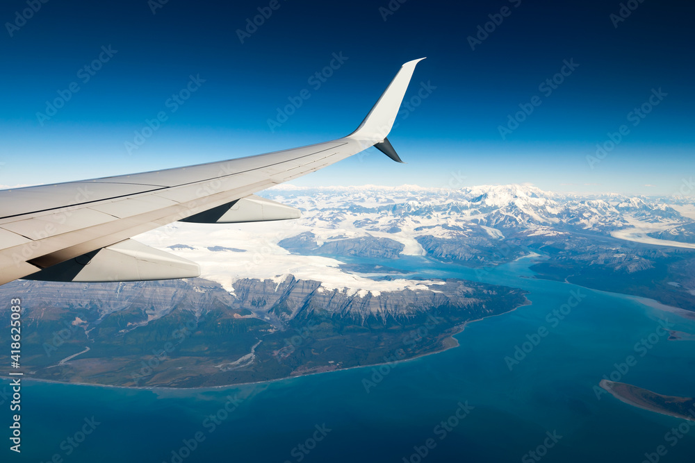 Airplane wing view with snow capped mountains in a cold environment. On board a Milk Run flight, between two small cities in the state of Alaska. Airplane wing view with snow capped mountains in a cold environment. On board a Milk Run flight, between two small cities in the state of Alaska.