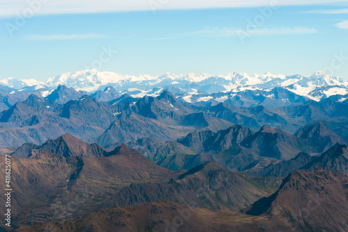 Aerial view of mountainous landscape in Alaska. Mountains with no snow in foreground and snow capped behind. Sunny day during summer.