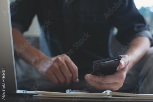 Man using mobile phone during online working on laptop computer at home office