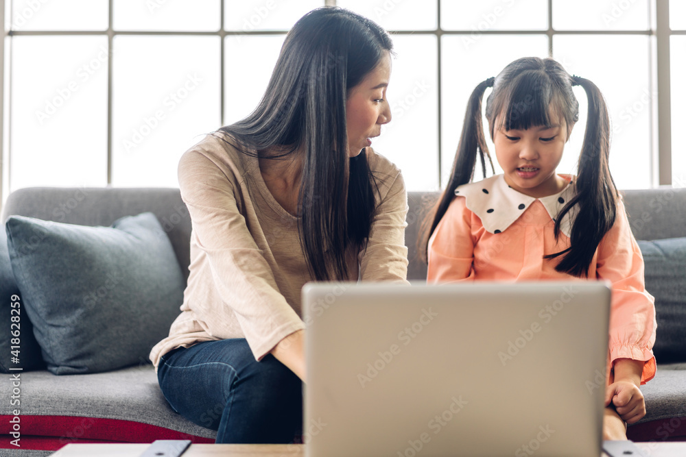 Mother and asian kid little girl learning and looking at laptop computer making homework studying knowledge with online education e-learning system.children video conference with teacher tutor at home Mother and asian kid little girl learning and looking at laptop computer making homework studying knowledge with online education e-learning system.children video conference with teacher tutor at home