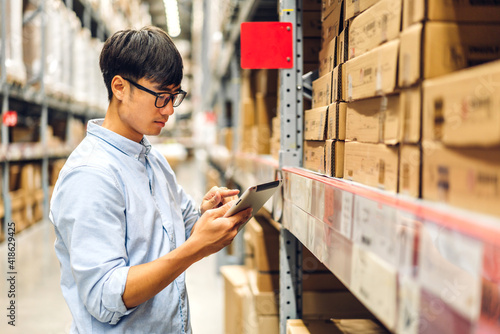 Portrait of smiling asian engineer foreman in helmets man order details checking goods and supplies on shelves with goods background in warehouse.logistic and business export © Art_Photo