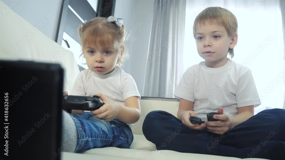 children play console in gamepads teamwork. kids a boy and a girl are playing a portable set-top box in a TV controller. happy family little lifestyle boy and girl have online fun games children play console in gamepads teamwork. kids a boy and a girl are playing a portable set-top box in a TV controller. happy family little lifestyle boy and girl have online fun games