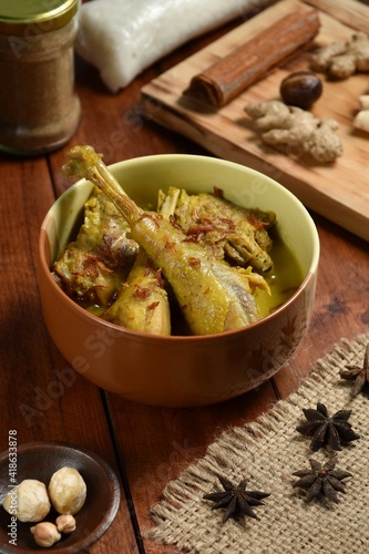 Opor Ayam is served on a wooden table. Opor is a traditional Indonesian food made from chicken cooked with coconut milk sauce