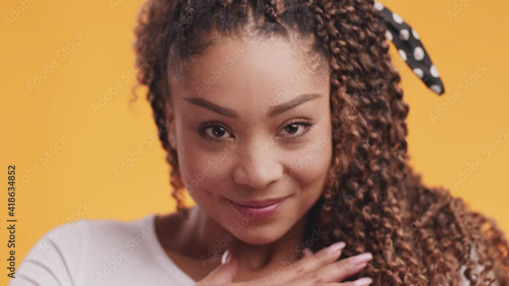 Close up portrait of young grateful african american woman touching her chest with gratitude, orange background Close up portrait of young grateful african american woman touching her chest with gratitude, orange background