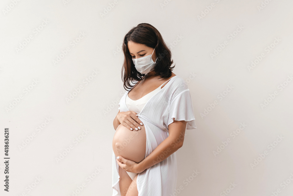 Young beautiful pregnant woman in medical surgical mask at home. Coronavirus, virus, isolation, stay at home. Young beautiful pregnant woman in medical surgical mask at home. Coronavirus, virus, isolation, stay at home.