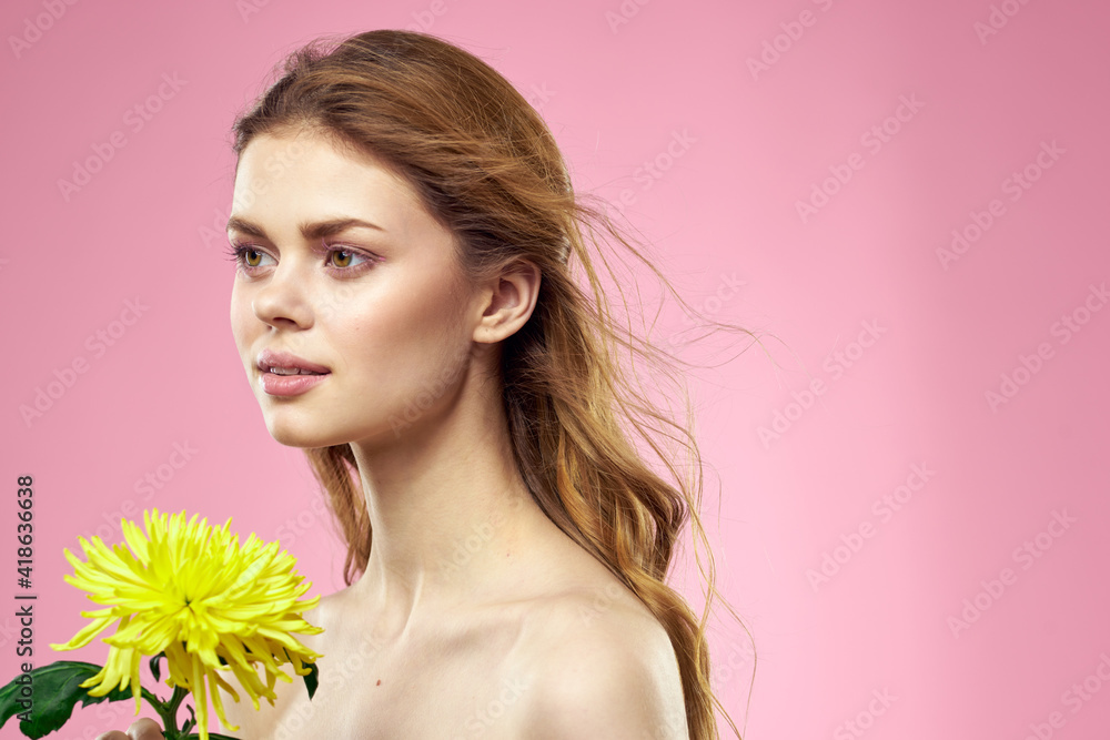 Beautiful girl with a yellow flower on a pink background nude shoulders makeup Beautiful girl with a yellow flower on a pink background nude shoulders makeup