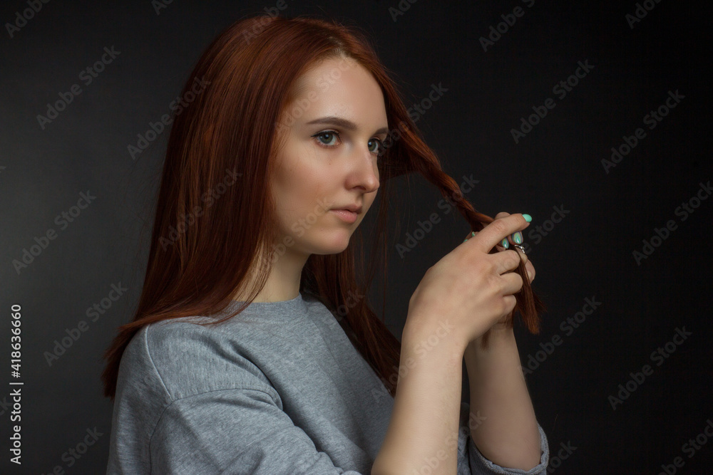 Red-haired young girl on black background in a gray T-shirt