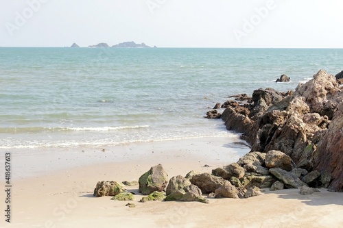 Sandy deserted beach with rocks jutting out into the ocean against a clear blue sky background