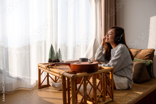 A beautiful young asian woman enjoy listening to music with headphone at home, happiness and relaxation concepts