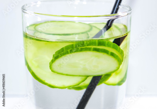 Detox water with a sliced cucumber in a glass with a straw for drinking. The concept of losing weight and cleansing the body. Macro.