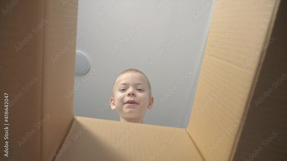 little boy opens a surprise parcel. kid lifestyle a opens cardboard box looking gift. child looks in the box is happy wonderment little boy opens a surprise parcel. kid lifestyle a opens cardboard box looking gift. child looks in the box is happy wonderment