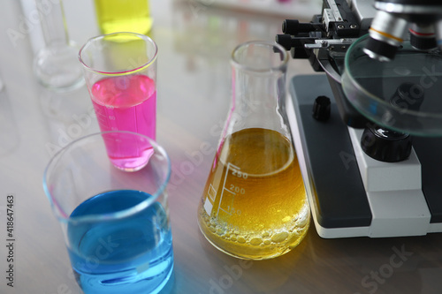 Chemical test tubes with multicolored liquid standing near microscope. Laboratory research concept