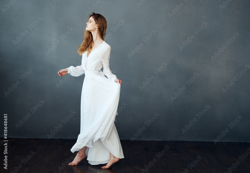 A romantic woman in a white dress in full growth is dancing on a gray background A romantic woman in a white dress in full growth is dancing on a gray background