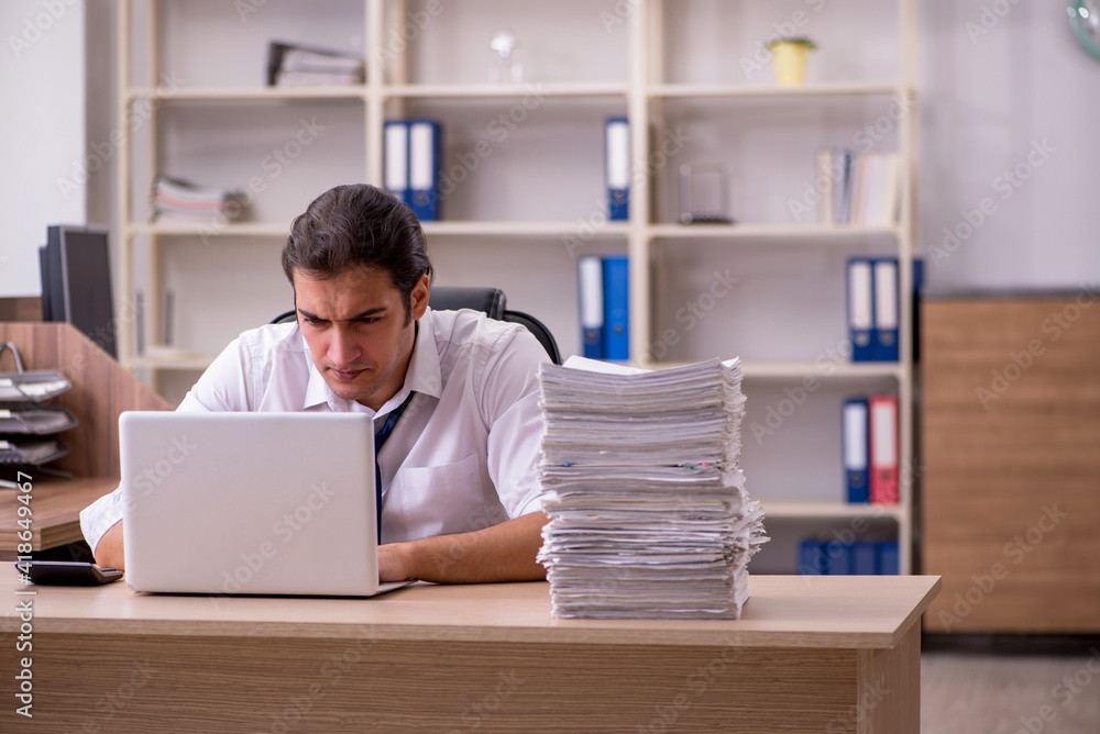 Young male employee unhappy with excessive work in the office Young male employee unhappy with excessive work in the office