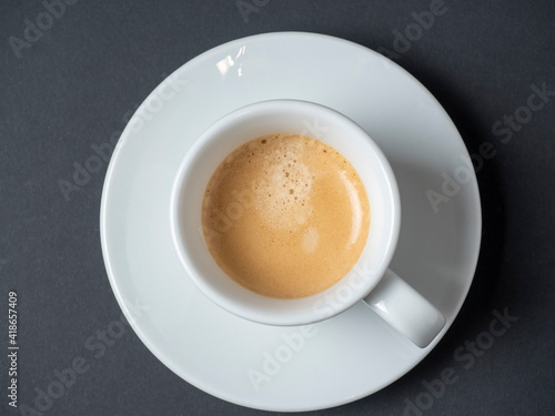 white cup with freshly brewed espresso on a dark background. Top view, flat lay, brown foam. Coffee concept