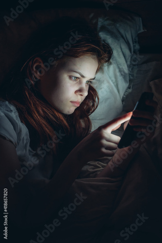 woman with a phone in her hands lying in bed at night addiction online