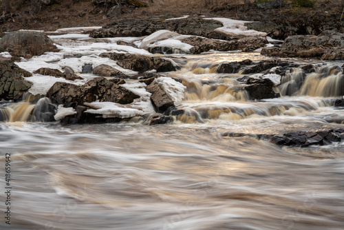 Water flowing over rocks with ice and sunlight on the water