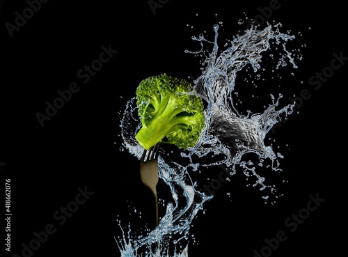 Nutrition and diet food picture with fresh broccoli on fork and water splash isolated on black background