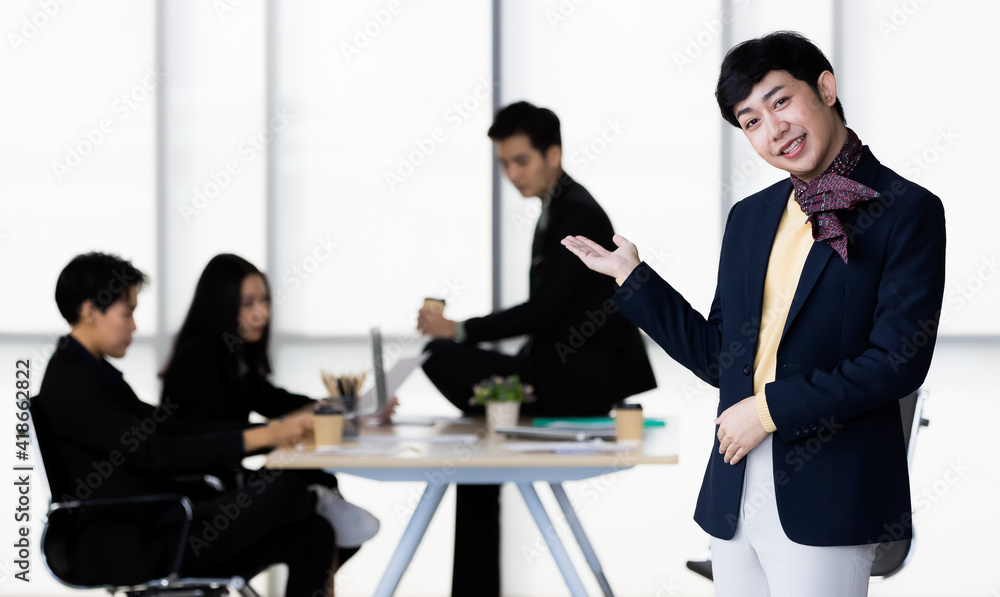 Portrait of LGBTQ transgender man office employee in casual suit standing and pose invite welcome gesture with cheerful and happy gesture with team colleagues blur in background Portrait of LGBTQ transgender man office employee in casual suit standing and pose invite welcome gesture with cheerful and happy gesture with team colleagues blur in background