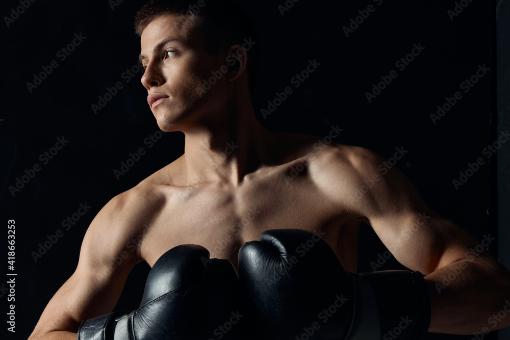 muscular boxer in black gloves on a dark background looking to the side 