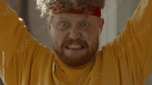 CARSH ZOOM Portrait of funny overweight Caucasian man working out with dumbbells at home, looking into camera. Bright, commercial high key advertising style lighting photo