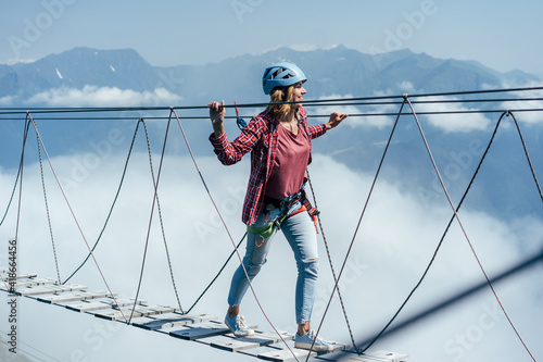 Fotografie A happy woman walks on a suspension bridge high in the mountains at the level of a cloud
