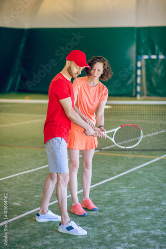 Tennis coach in red cap training a dark-haired woman