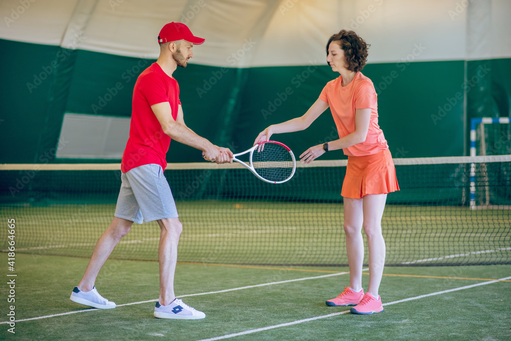 Man in a red cap and with a racket having a workout with his female coach