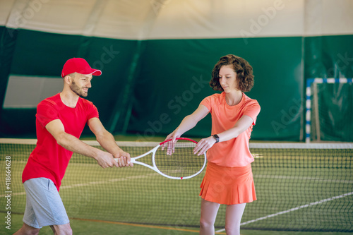 Man in a red cap and with a racket having a workout with his female coach