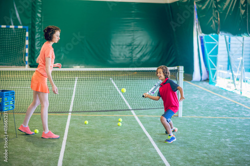 Female coach in bright clothes playing tennis with a boy