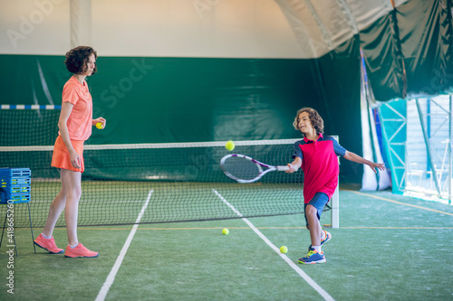 Female coach in bright clothes playing tennis with a boy