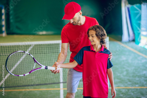 Male tennis coach showing a boy how to hold the racket