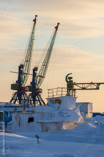Winter view of the cranes of a small cargo seaport in the far north of Russia in the Arctic. Hammer and sickle (symbol of the Soviet Union). A lot of snow. Cold weather. Chukotka, Siberia, Russia. photo