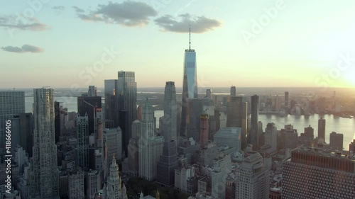 Aerial shot of skyscrapers in financial district against sky, drone flying forward towards famous One World Trade Center in city during sunset - New York City, New York