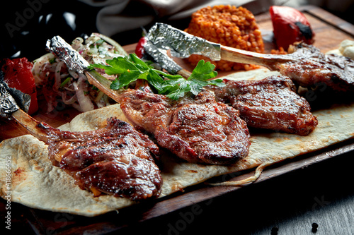 Lamb rack cooked on the grill with pita bread, bulgur and grilled vegetables on a wooden board. Turkish shashlik. Close up, selective focus