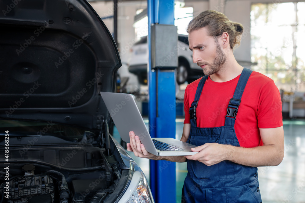 Serious man with computer near car in garage