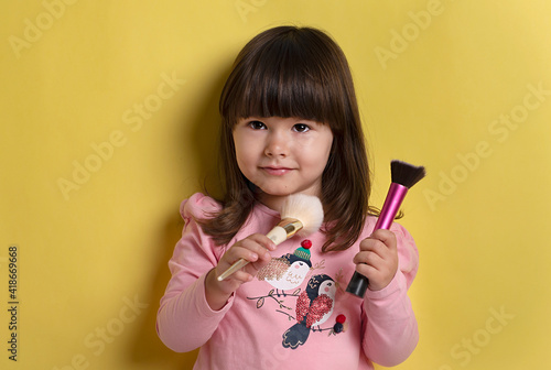 Natural cosmetics for kids. happy little girl create her image. female beauty and fashion. small girl apply  with makeup brush. put blush on. cheerful child has trendy hair braids