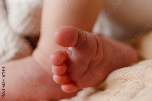 A close-up of the baby's foot. Small foot of a man with small toes and tiny nails on the background of a beige bedspread