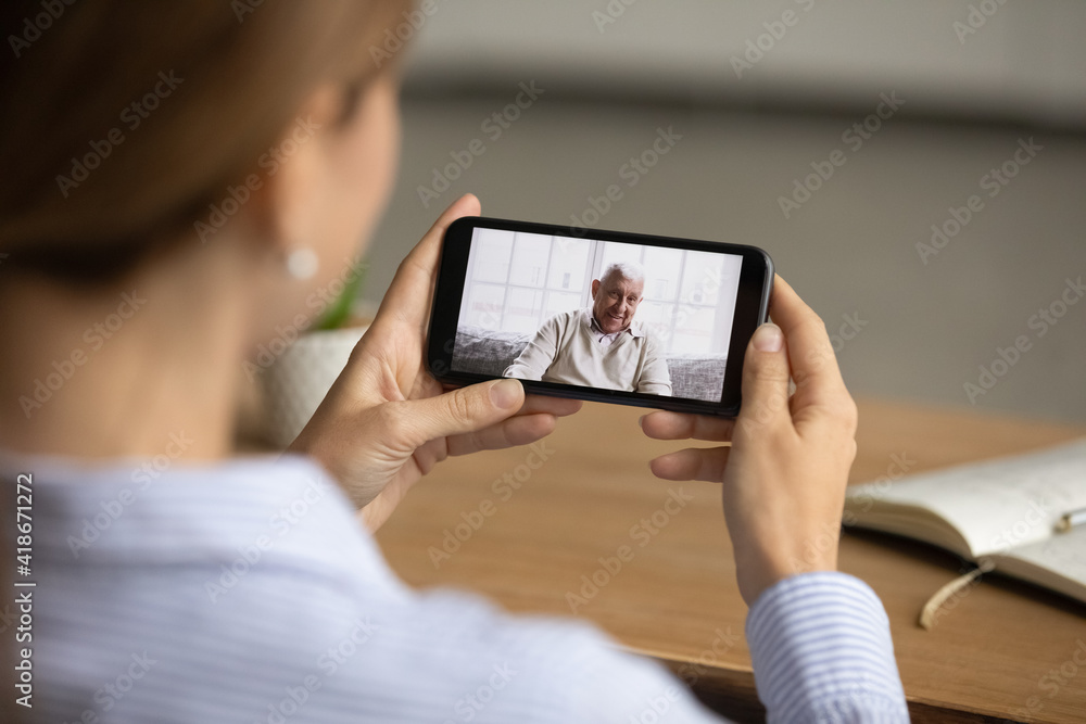 Back view close up of woman hold smartphone talk speak on video call with elderly father. Female have webcam digital online conversation with mature dad using cellphone. Family communication concept.
