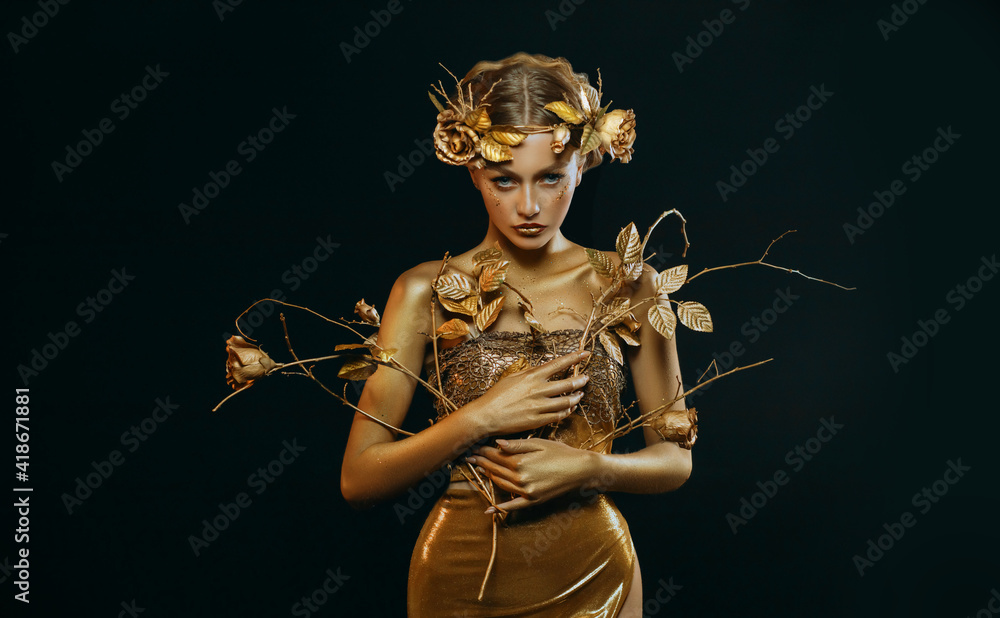 Beauty fantasy woman, face in gold paint. Golden shiny skin. Fashion model girl, image goddess. Glamorous crown, wreath roses, jewellery accessories. Professional metallic makeup. hand holds a branch. - obrazy, fototapety, plakaty 